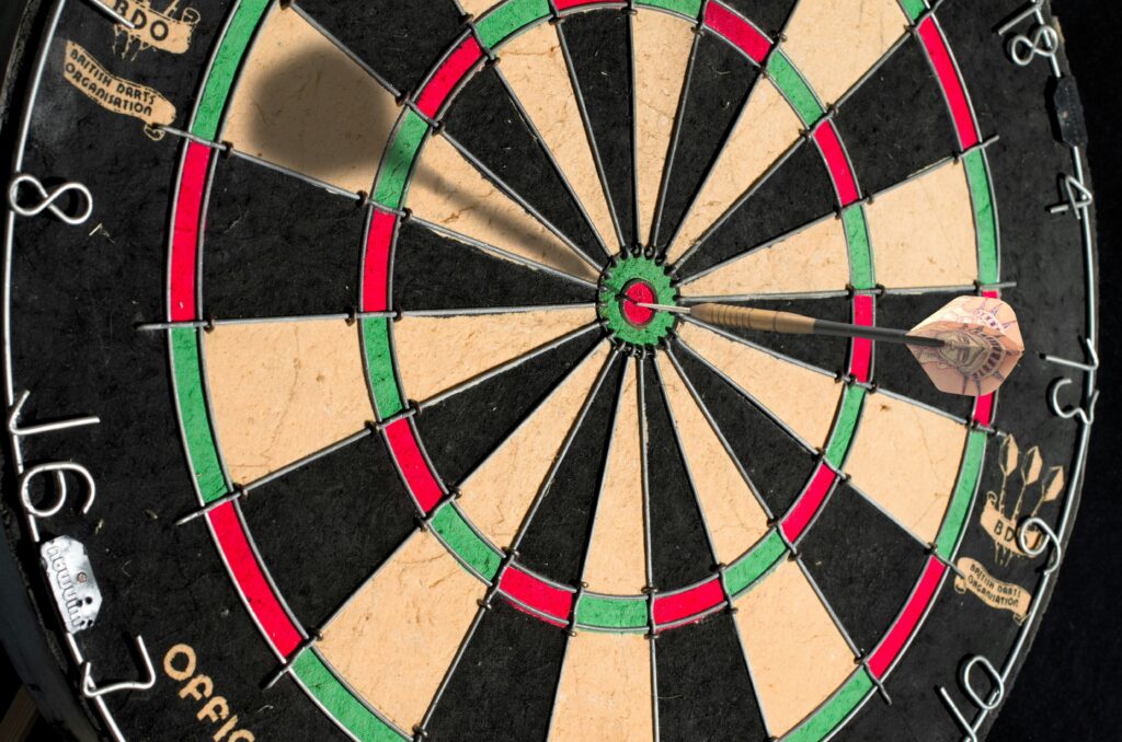 A dartboard with a dart hitting the bullseye. The board has black, white, red, and green sections, with numbers around the edge. The dart is embedded in the center red circle.