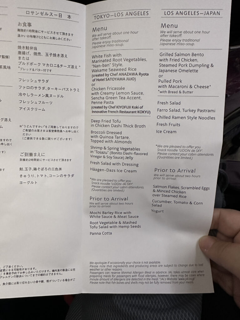 The image shows an airline menu for flights between Tokyo and Los Angeles, and Los Angeles to Japan. It includes meal options for each route, with dishes like white fish with marinated root vegetables, chicken fricassée, grilled salmon bento, and pulled pork with macaroni and cheese. There are also options for prior to arrival, such as mochi barley rice and salmon flakes with scrambled eggs. The menu includes notes about meal availability and allergen information. The text is in both English and Japanese.
