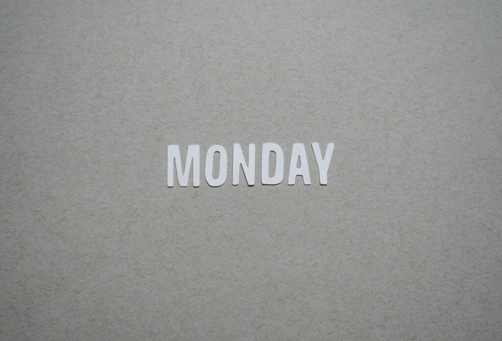 The image shows the word "MONDAY" in white capital letters on a textured gray background.