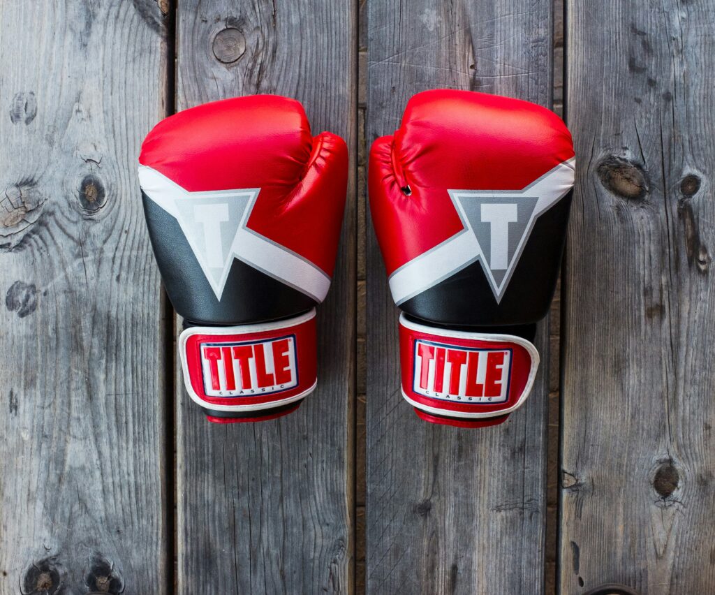 A pair of red boxing gloves with black and white accents, featuring the brand name "Title" on the wrist straps, are placed side by side on a wooden surface.