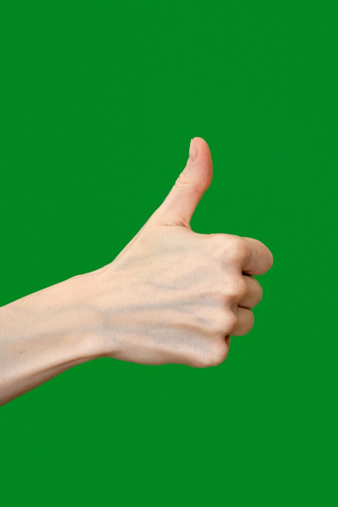 A hand giving a thumbs-up gesture against a solid green background.