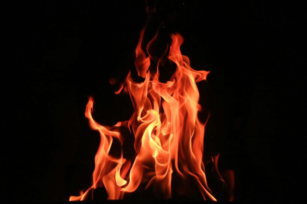 A close-up image of bright orange and yellow flames against a dark background. The flames are twisting and curling upwards, creating a dynamic and intense visual effect.