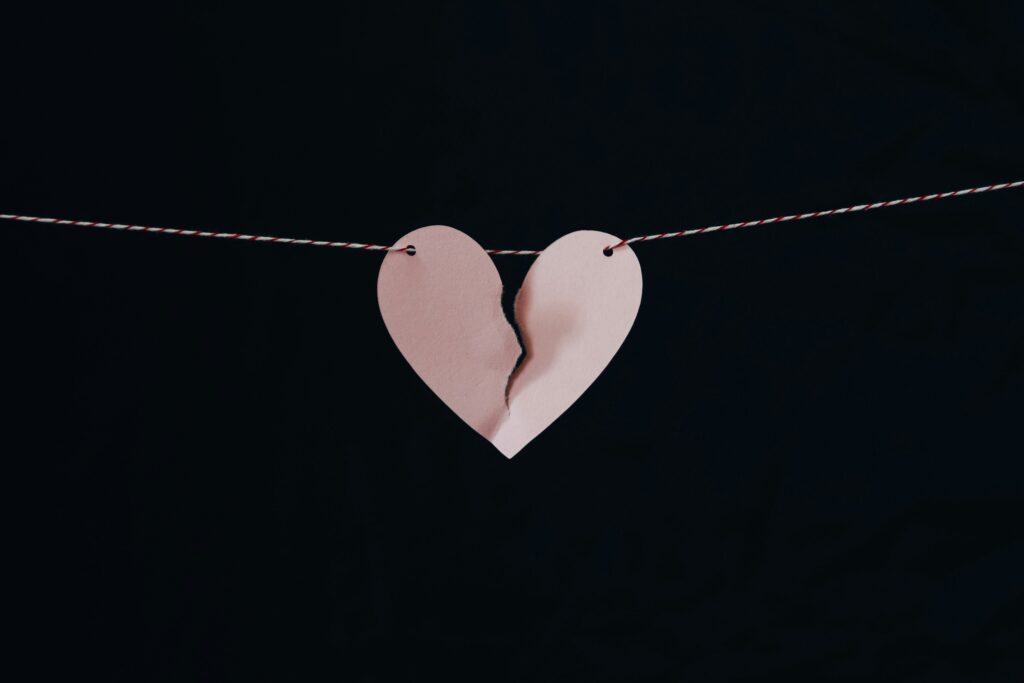 A torn paper heart hanging on a string against a dark background.