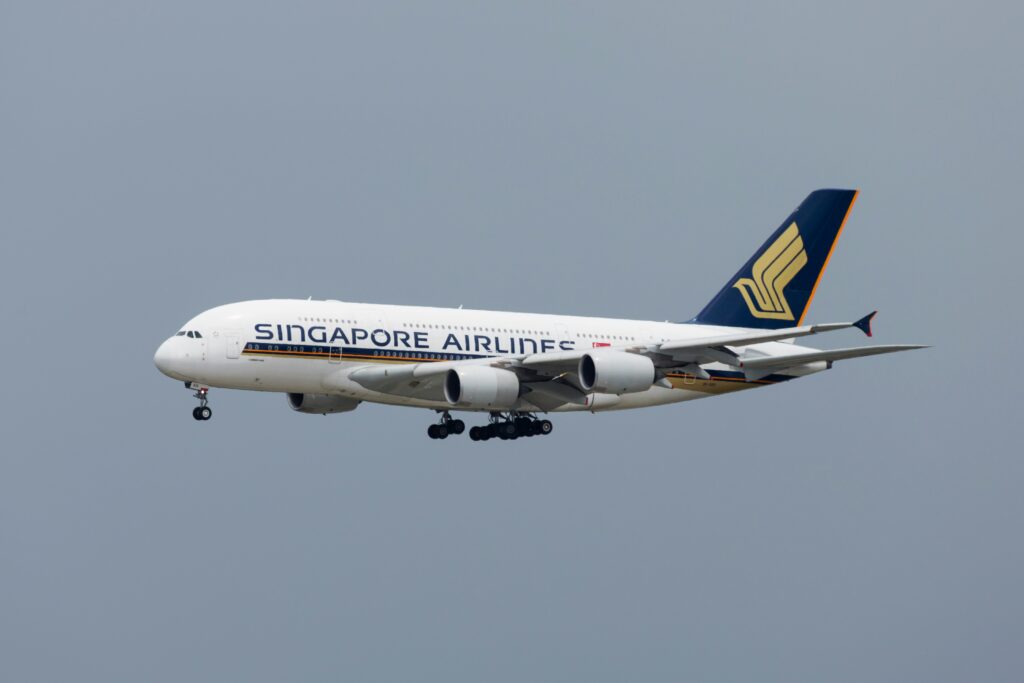An airplane in flight with "Singapore Airlines" written on the side. The aircraft is a large passenger jet with its landing gear extended, flying against a clear sky.